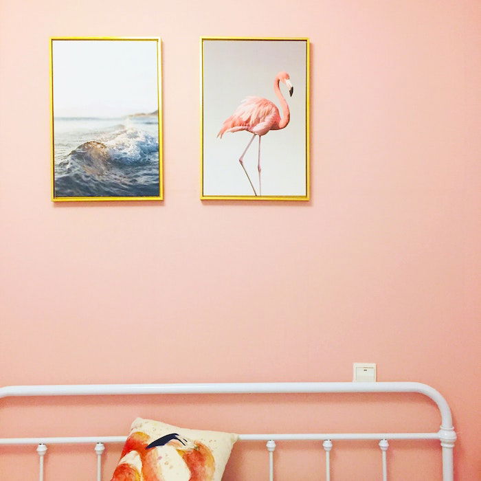 Enlarged printed and framed photos of the ocean and a flamingo hung above a bed frame