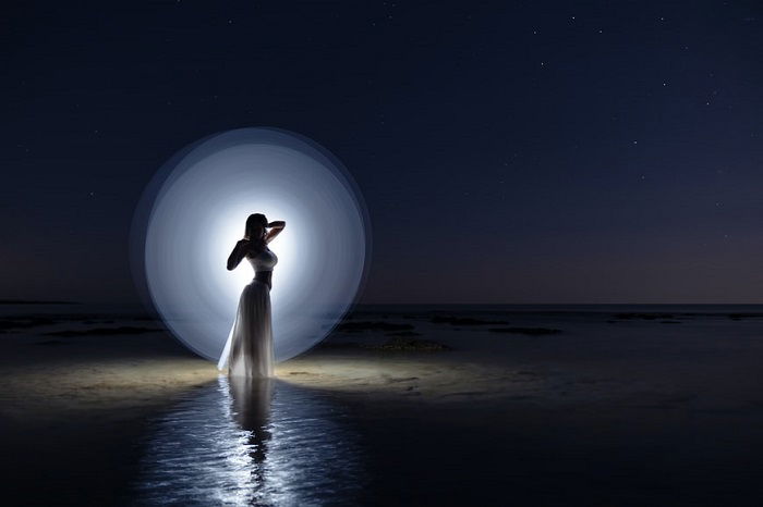 Night light painting with a white light imitating the moon behind a woman 