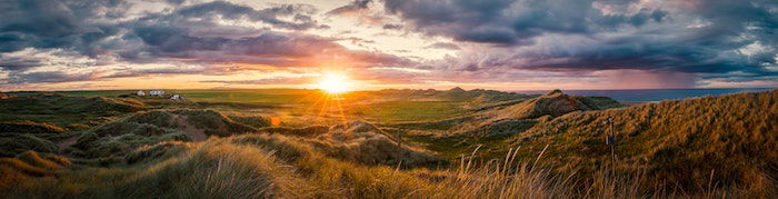 Panorama landscape image of clouds a setting sun and vast land of grassland and ridges