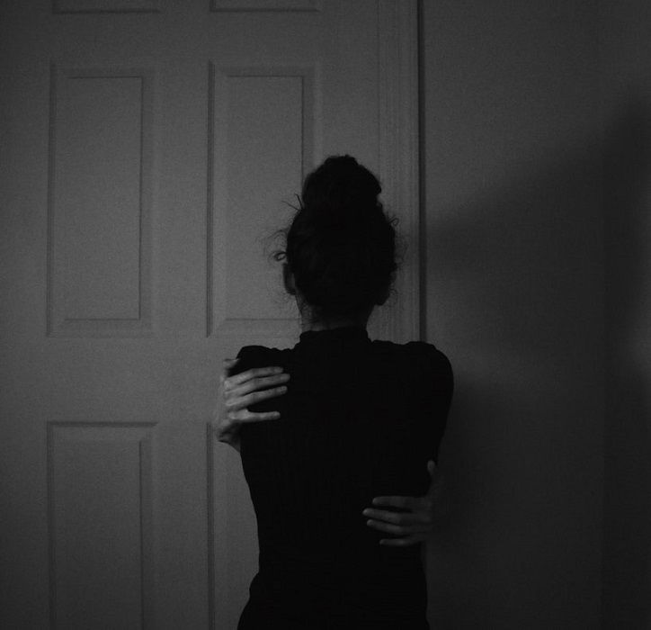 A woman in a dark room holding onto a door with her back to the camera.