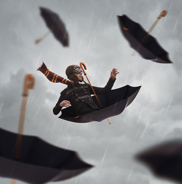 A man riding an umbrella in the rain, with multiple umbrellas falling around him. 