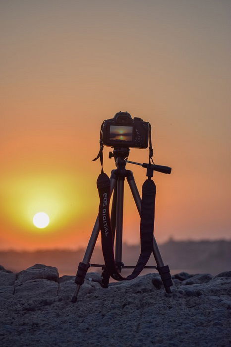 camera on a tripod aimed at a sunset 