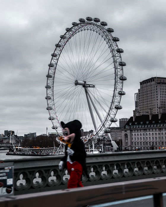 A photo of the London Eye in the background with a blurred person in a Mickey Mouse costume walking by in the foreground