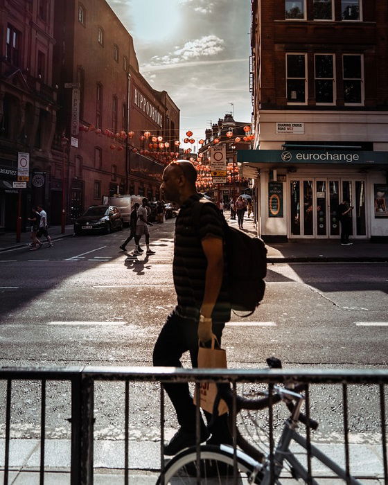 A backlit photo of a man walking by on the sidewalk on a sunny day