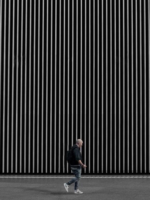 A man walking by a large wall with thin graphic white lines on a black background