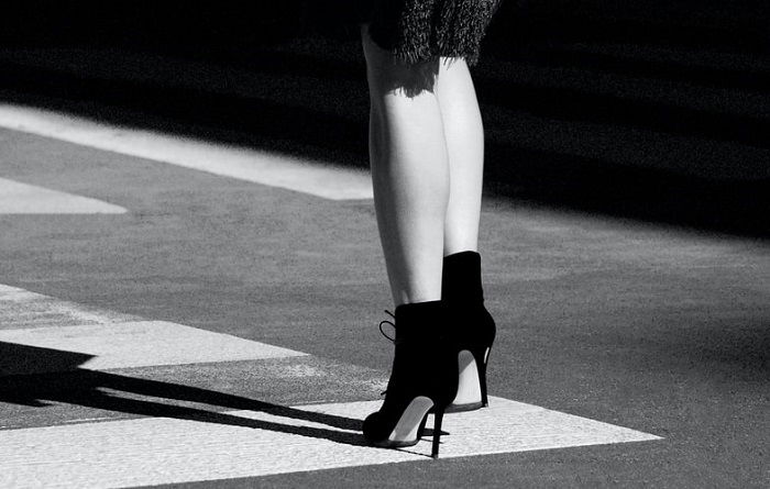 A black-and-white abstract photo of a woman's lower legs and feet in high heels on a street sidewalk