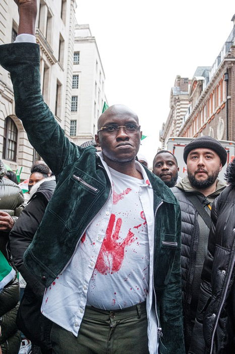 A Black man with his arm lifted in the air as a sign of protest waling with a group of people in the street