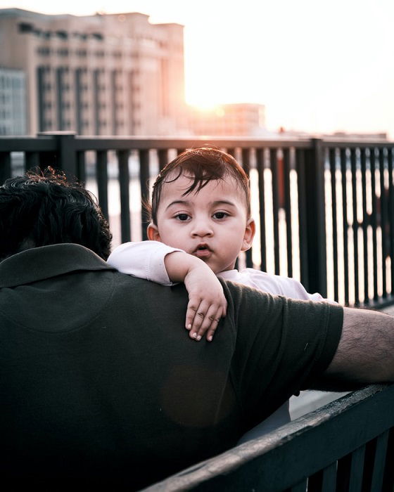 A street portrait of a child looking over the shoulder of a man