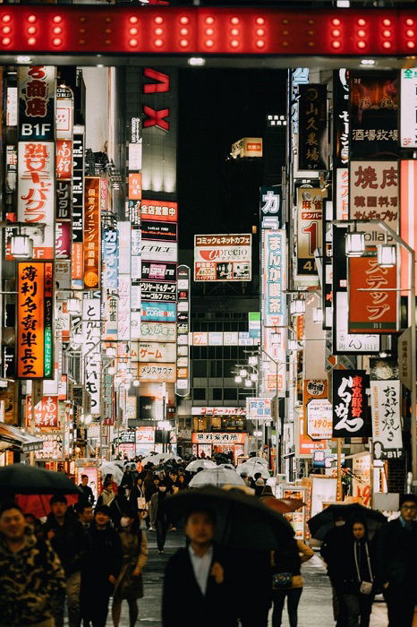 People with umbrellas walking down a pedestrian street in Japan filled with store signs at night