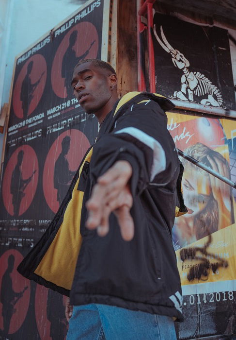 A fashion street photo of a man with an urban background and his hand reaching down to the camera