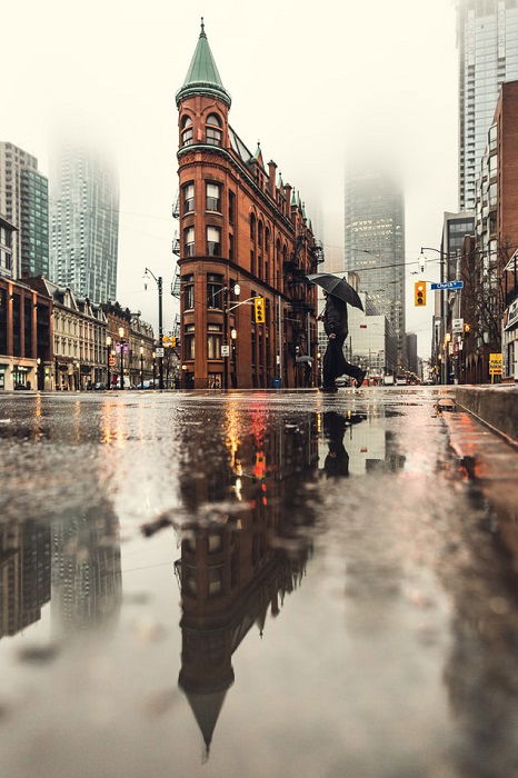 A low-perspective shot of a building and its reflection in puddles on a rainy street scene