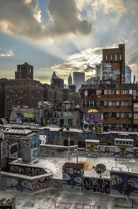 sun peeking through clouds over a rooftop full of graffiti 