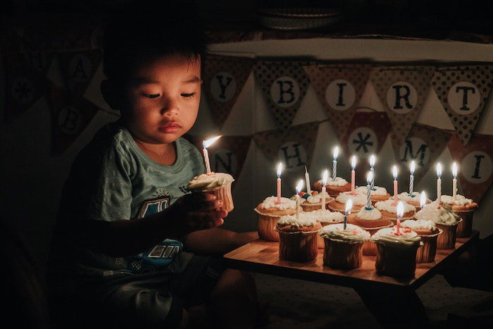 Child holding cupcake with lit candle and tray of cupcakes with lit candles