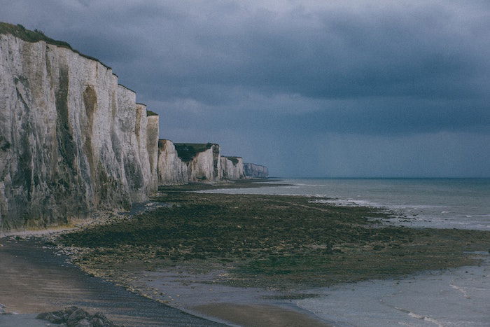 Low contrast landscape image of a coastline with cliffs, a beach, and water