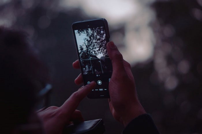 A finger about to touch a shutter button on an Android camera phone to take a dark tree image for smartphone photography