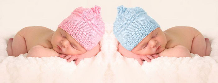 newborn twins photography: newborn twins in pink and blue knitted hats posed with their heads resting on their crossed arms