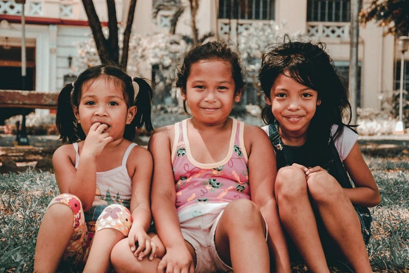 photo ideas for siblings: siblings siting on a lawn with buildings in the background