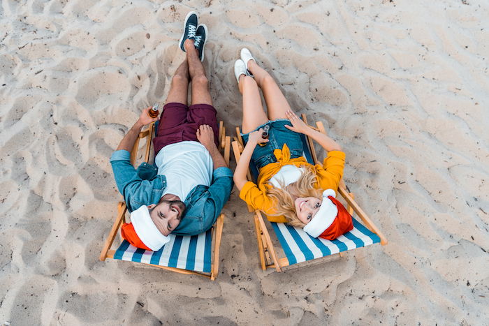 A couple wearing Santa hats and sitting in beach chairs for Christmas card photo ideas