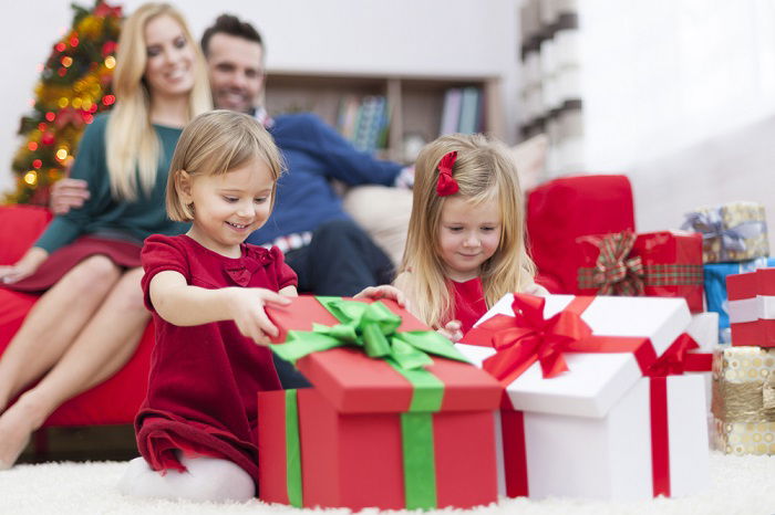 a couple watches their two daughters open their Christmas presents 