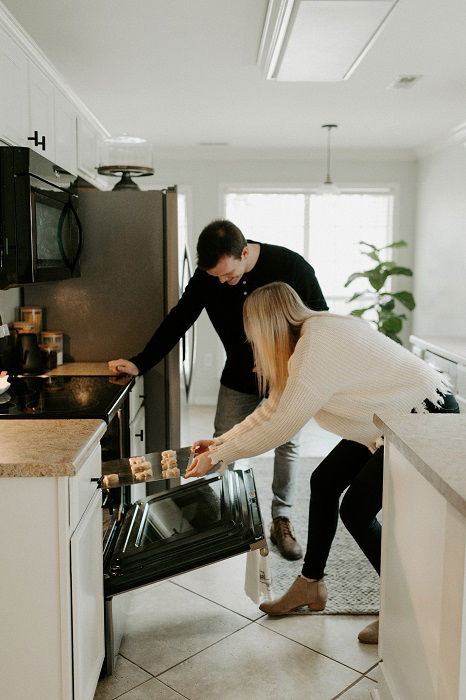 christmas couple photoshoot ideas: a man and woman putting Christmas cookies in the oven together 