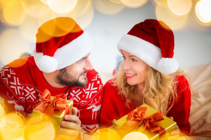 a couple photographed in Santa hats and Christmas sweaters look into each others eyes