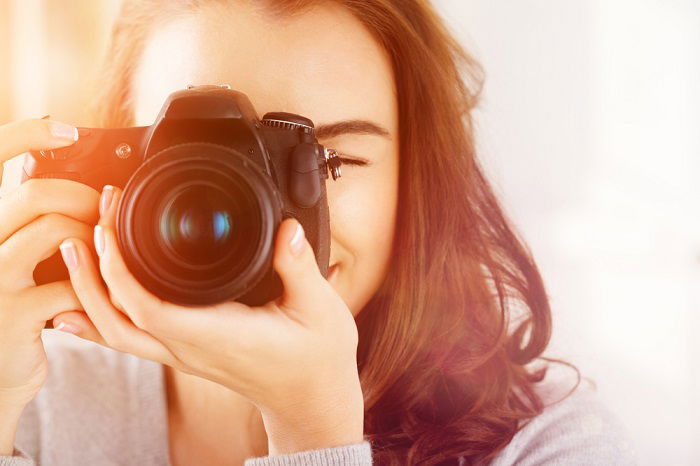 a head on shot of a woman pointing a camera at the photographer taking the photo