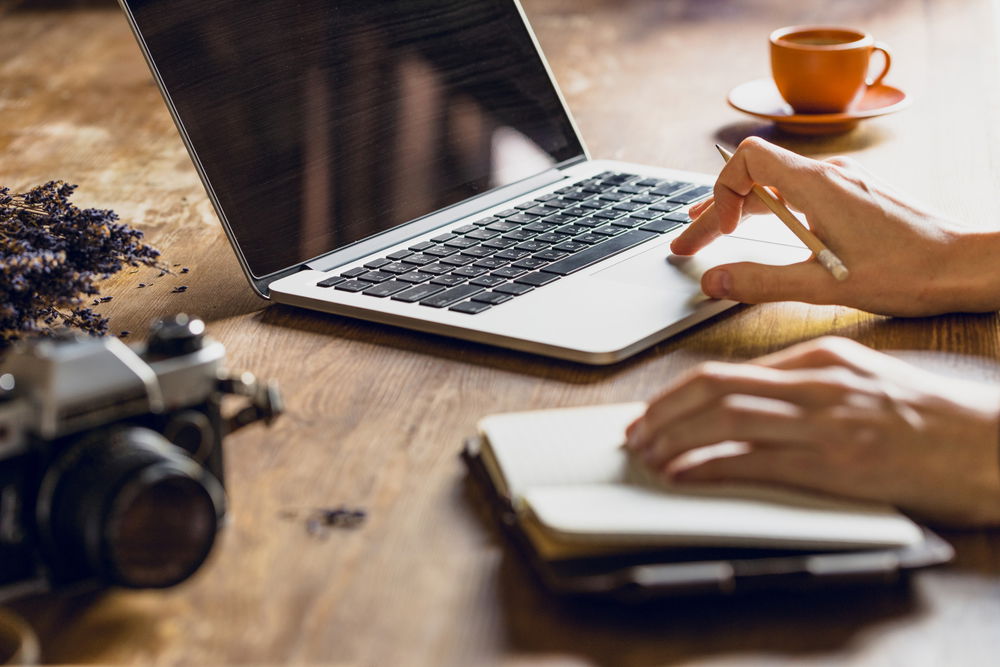 a photographer taking notes from their notebook and typing them on their laptop