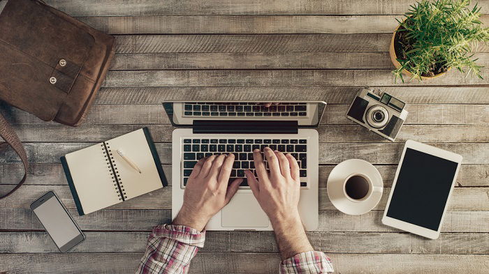 a flat lay photo of someone typing on their laptop on a wooden table