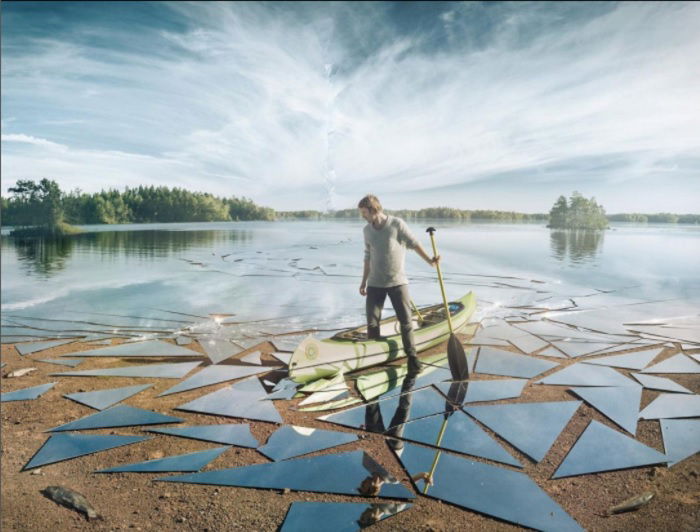 A photo of a man standing with one leg in a canoe and the other holding a paddle on a lake with water turned into shards of glass for creative editing ideas