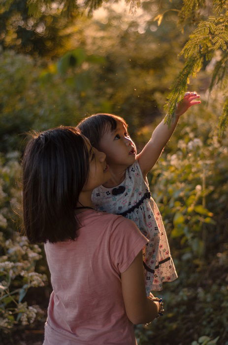 One girl carrying a baby girl in a wooded area as a sister photoshoot idea