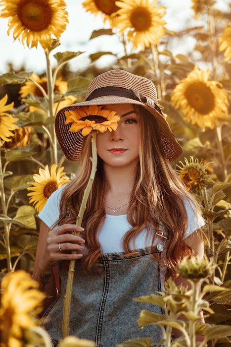 A model surrounded by sunflowers holding a sunflower to her face 