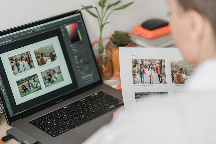 an image of a man looking at a macbook screen and comparing images to a printout