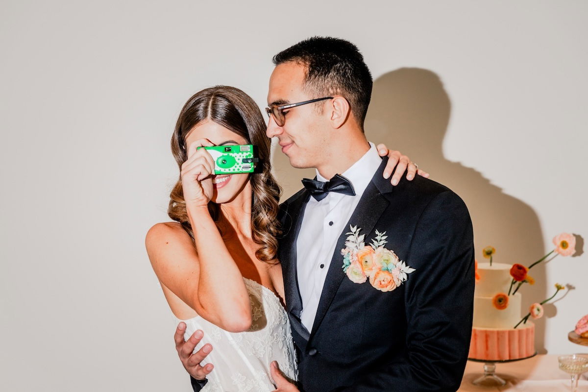 A groom looking at his bride taking a picture with an instant camera