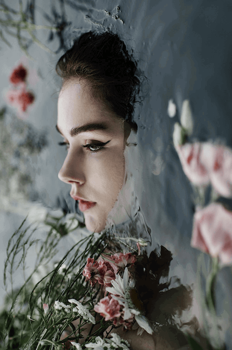 A woman's face above water surrounded by flowers and foliage