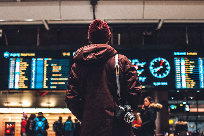 Travel photographer standing in an aiport with a camera slung over their shoulder