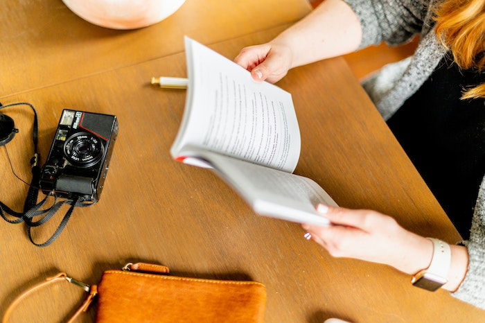 A person reading a book with a point-and-shoot camera on the table