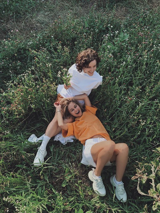 Two girls sitting in a meadow one with her head in the other's lap