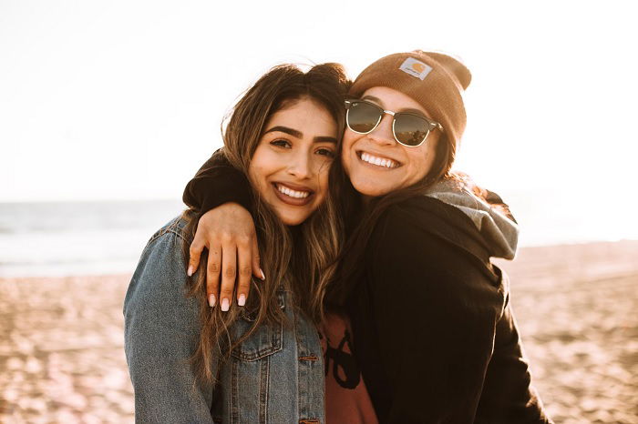 Two female friends standing close on a beach as an idea for a best friend photoshoot