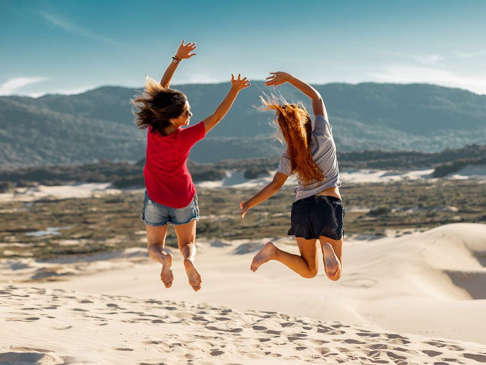 Two women jumping on a sand dune