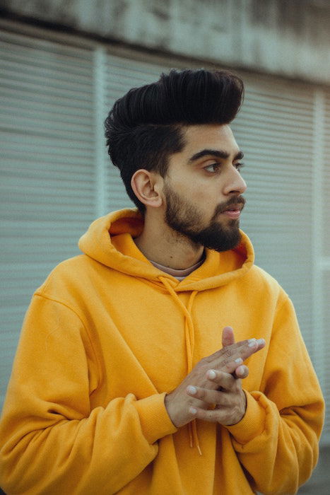 Man in yellow hoodie with hands together and neutral facial expression as an idea for male poses