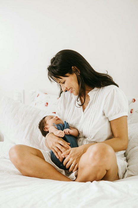 A mother sitting on a bed with baby in her arms as an inspiration for newborn photography