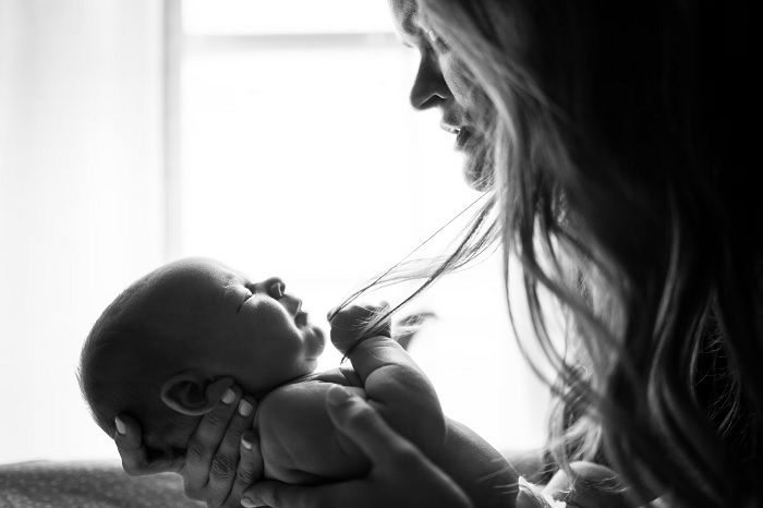 Black and white photo of mother holding baby in front of her an an example of newborn photography