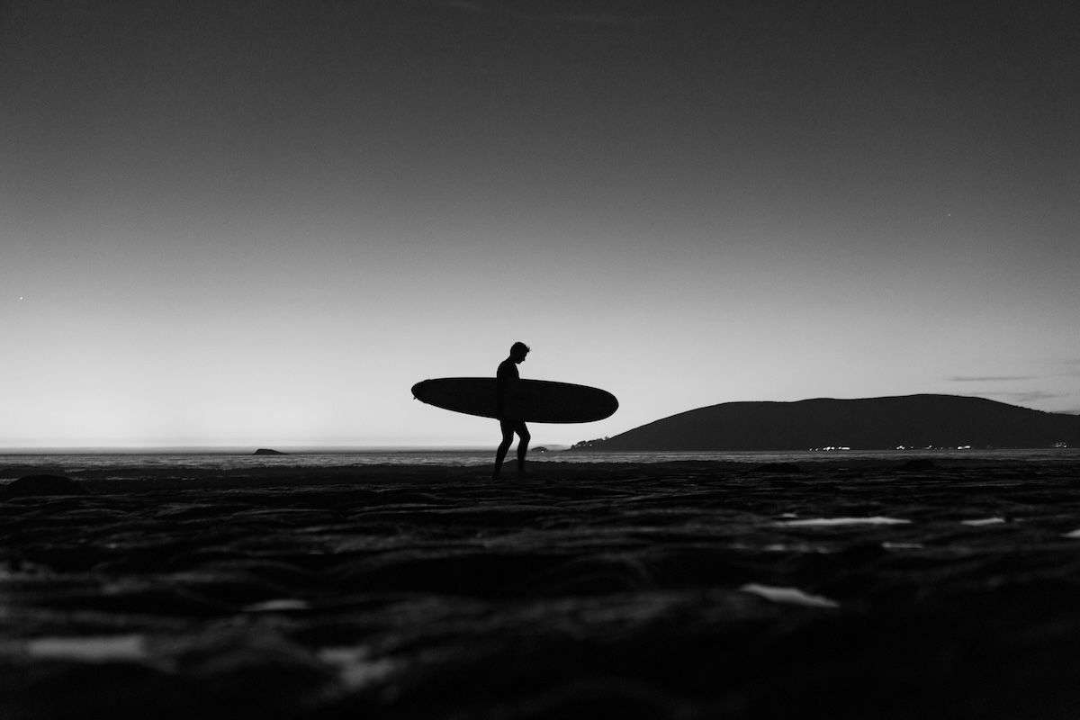 A black-and-white silhouette of a surfer carrying a surfboard from the water as an example of surf photography