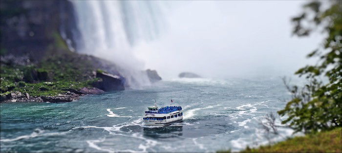 A tilt shift photography shot of a boat before a waterfall