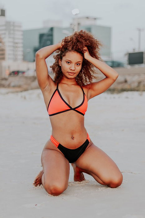 Girl kneeling on the beach with her hands in her hair as an idea for bikini poses