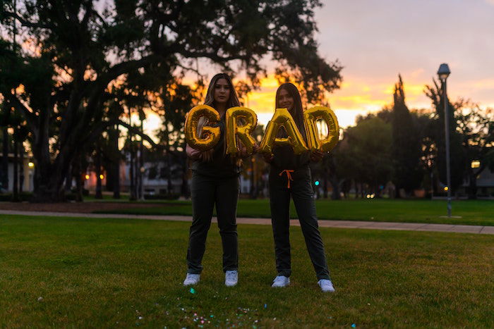 Two people posing in front of a sunset with the word grad in giant letters.