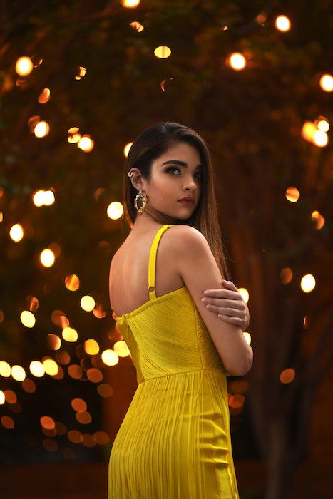 Three-quarter portrait of a girl in a yellow dress looking over her shoulder with bokeh in the background