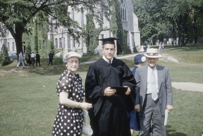 Vinatage-looking photo of a graduate posing in a park with his parents