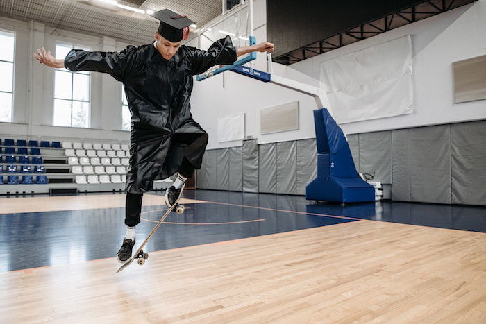 Senior high-school graduate doing a trick on a skateboard in a gymnasium