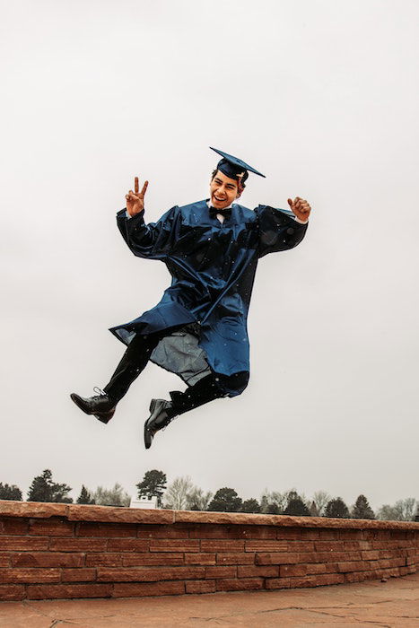 Senior high-school graduate jumping in the air flashing a peace sign